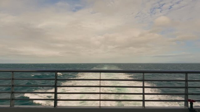 Railing frames a turbulent ocean under a cloudy sky. Waves crash against the horizon with relentless energy. The scene suggests motion, power, and the vastness of the sea. Perfect for adventure
