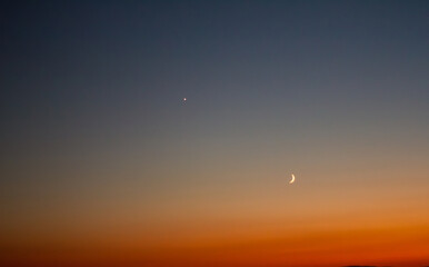 Horizontal eye level wide shot of crescent moon and Venus planet in clear sunset sky gradient © Alexander