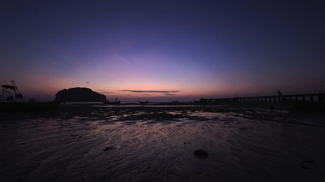 Twilight over tropical white sand beach with tidal flats, pier and palm trees