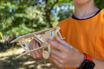 A boy plays with a wooden model of an airplane in a park, pointing at the airplane's propeller. © Prrrettty