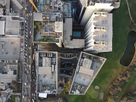 Aerial view of modern high-rise buildings with rooftop HVAC units, a busy road with traffic, and a green golf course with a pond in Santiago de Surco, Lima Province, Peru.