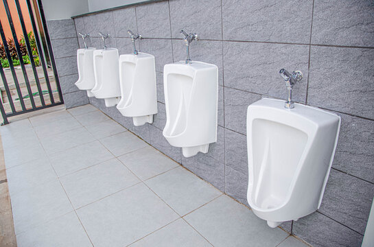 Row of clean white ceramic urinals in a modern public male restroom with grey tile wall.