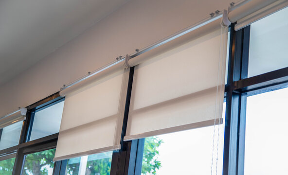 White roller blinds installed on large glass windows in modern room.Modern white roller shades for sun protection on office glass window background.