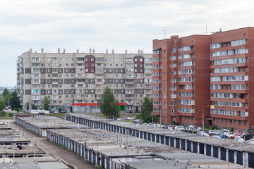 Obraz premium Residential apartment buildings stand alongside garages and a parking area, with green trees and a cloudy sky visible in the urban landscape