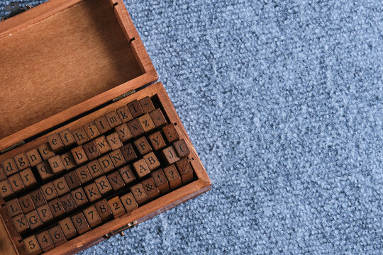 Wooden box filled with rubber stamp letters and numbers, placed on grey carpet with copy space on right.