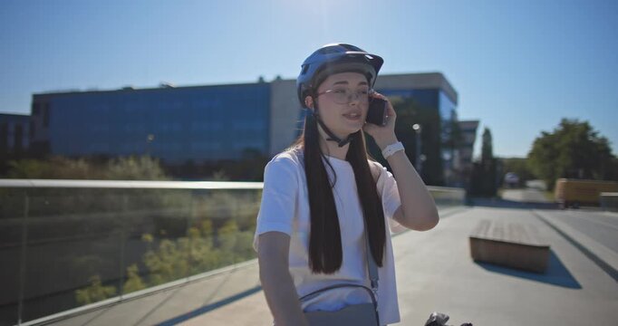 A young beautiful girl in casual clothes rides a bicycle on a bridge in the city in the morning during blue hour