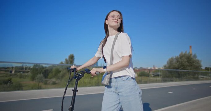 A young beautiful girl in casual clothes rides a bicycle on a bridge in the city in the morning during blue hour
