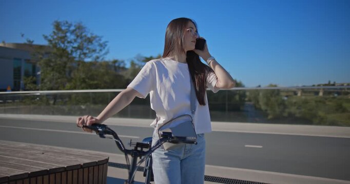 A young beautiful girl in casual clothes rides a bicycle on a bridge in the city in the morning during blue hour