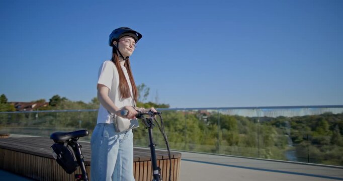 A young beautiful girl in casual clothes rides a bicycle on a bridge in the city in the morning during blue hour