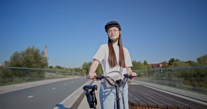 A young beautiful girl in casual clothes rides a bicycle on a bridge in the city in the morning during blue hour