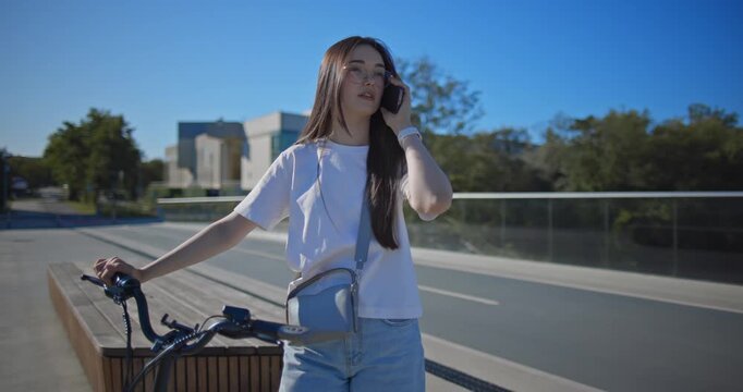 A young beautiful girl in casual clothes rides a bicycle on a bridge in the city in the morning during blue hour