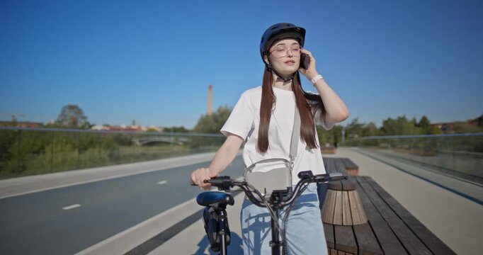 A young beautiful girl in casual clothes rides a bicycle on a bridge in the city in the morning during blue hour