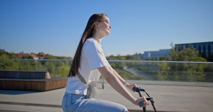 A young beautiful girl in casual clothes rides a bicycle on a bridge in the city in the morning during blue hour