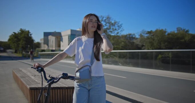 A young beautiful girl in casual clothes rides a bicycle on a bridge in the city in the morning during blue hour