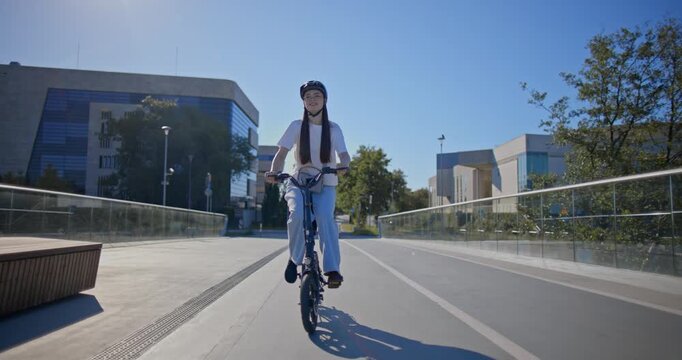 A young beautiful girl in casual clothes rides a bicycle on a bridge in the city in the morning during blue hour