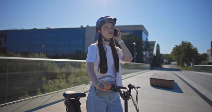 A young beautiful girl in casual clothes rides a bicycle on a bridge in the city in the morning during blue hour
