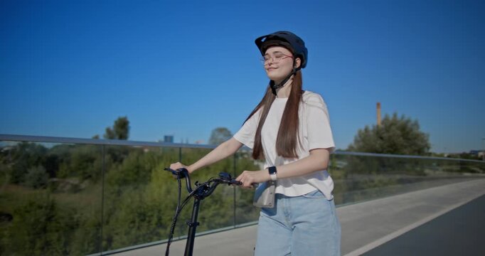 A young beautiful girl in casual clothes rides a bicycle on a bridge in the city in the morning during blue hour