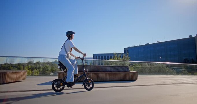A young beautiful girl in casual clothes rides a bicycle on a bridge in the city in the morning during blue hour
