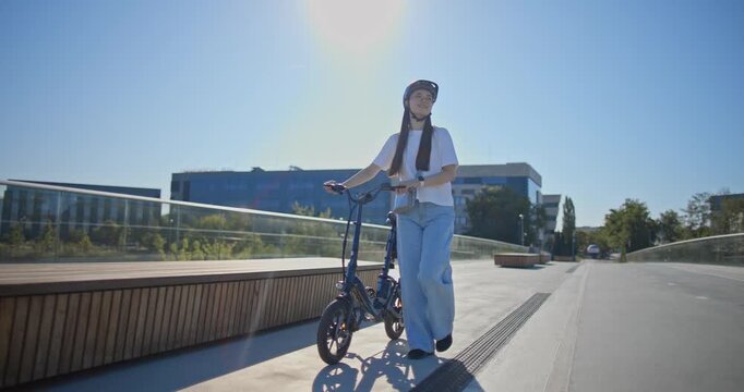 A young beautiful girl in casual clothes rides a bicycle on a bridge in the city in the morning during blue hour