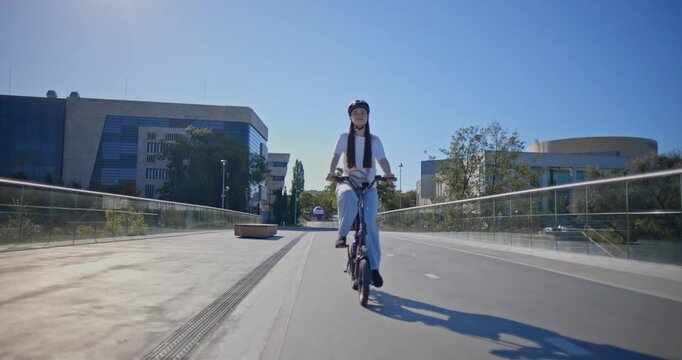 A young beautiful girl in casual clothes rides a bicycle on a bridge in the city in the morning during blue hour
