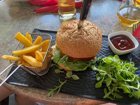 Burger mit Salat, K&auml;se und Sauce, serviert mit knusprigen Pommes frites im Metallkorb. Restaurantgericht, Fast Food, Street Food, Mittagessen und authentische Food-Fotografie.