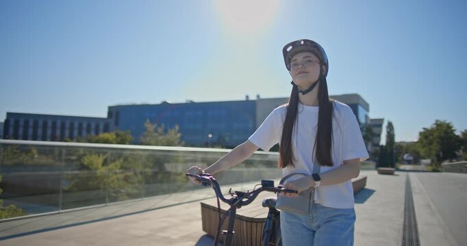 A young beautiful girl in casual clothes rides a bicycle on a bridge in the city in the morning during blue hour