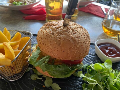 Burger mit Salat, K&auml;se und Sauce, serviert mit knusprigen Pommes frites im Metallkorb. Restaurantgericht, Fast Food, Street Food, Mittagessen und authentische Food-Fotografie.
