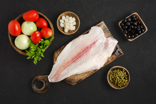 Fresh pangasius fish fillet and vegetables on wooden cutting board in kitchen
