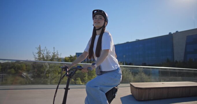 A young beautiful girl in casual clothes rides a bicycle on a bridge in the city in the morning during blue hour