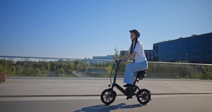 A young beautiful girl in casual clothes rides a bicycle on a bridge in the city in the morning during blue hour