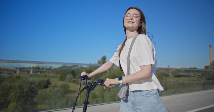 A young beautiful girl in casual clothes rides a bicycle on a bridge in the city in the morning during blue hour
