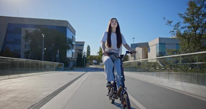 A young beautiful girl in casual clothes rides a bicycle on a bridge in the city in the morning during blue hour
