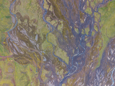 Aerial view of braided river system with dark volcanic sediment and vibrant green mossy terrain in Iceland.