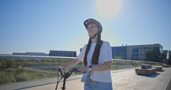 A young beautiful girl in casual clothes rides a bicycle on a bridge in the city in the morning during blue hour