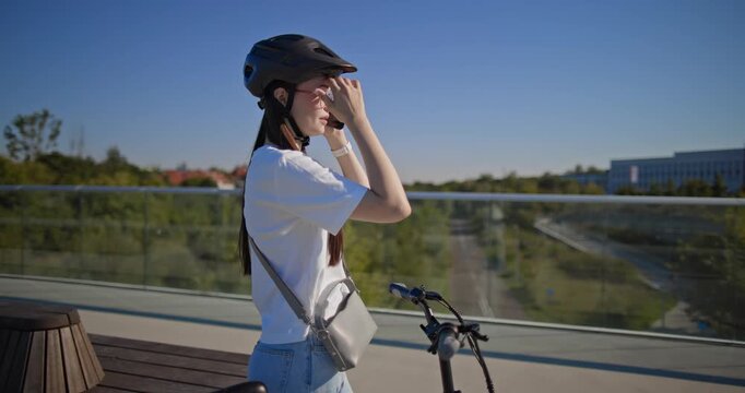 A young beautiful girl in casual clothes rides a bicycle on a bridge in the city in the morning during blue hour