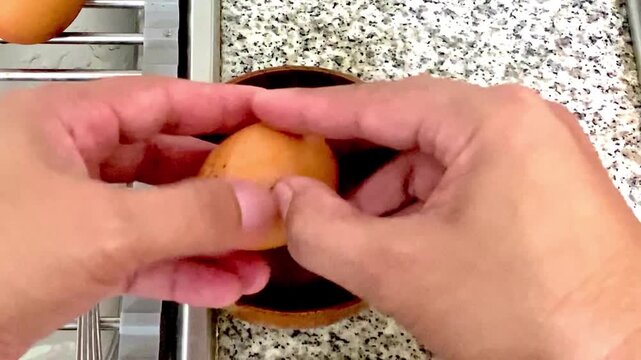   Close-up of hands carefully peeling the shell from a soft boiled onsen egg and placing the cooked egg into a small bowl.