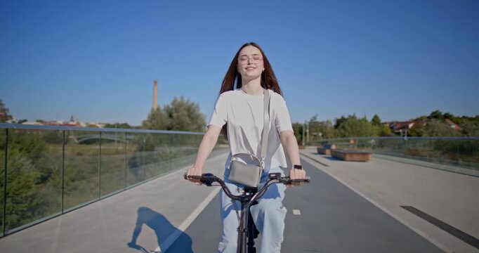 A young beautiful girl in casual clothes rides a bicycle on a bridge in the city in the morning during blue hour
