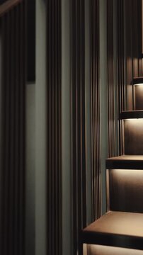 Vertical video. Illuminated modern stairs with warm linear lights and a dark metal railing.