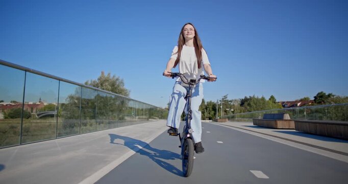 A young beautiful girl in casual clothes rides a bicycle on a bridge in the city in the morning during blue hour
