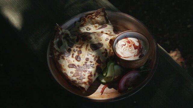 Golden folded crepe stuffed with melted cheese and served with creamy dipping sauce and fresh vegetables on a rustic wooden plate. Cinematic close-up in natural sunlight with shallow depth of field.