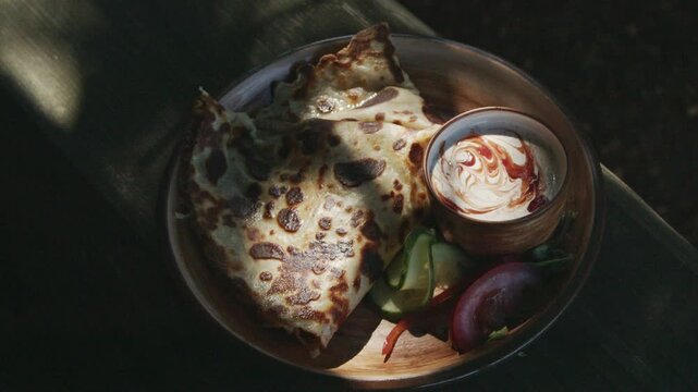 Golden folded crepe stuffed with melted cheese and served with creamy dipping sauce and fresh vegetables on a rustic wooden plate. Cinematic close-up in natural sunlight with shallow depth of field.