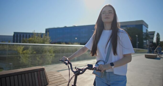 A young beautiful girl in casual clothes rides a bicycle on a bridge in the city in the morning during blue hour