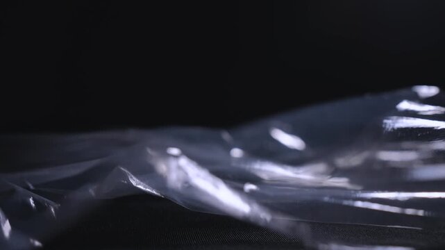 A transparent polyethylene sheet billows in wind, forming glossy folds on a black background. Concept packaging, material texture, abstract design and advertising.