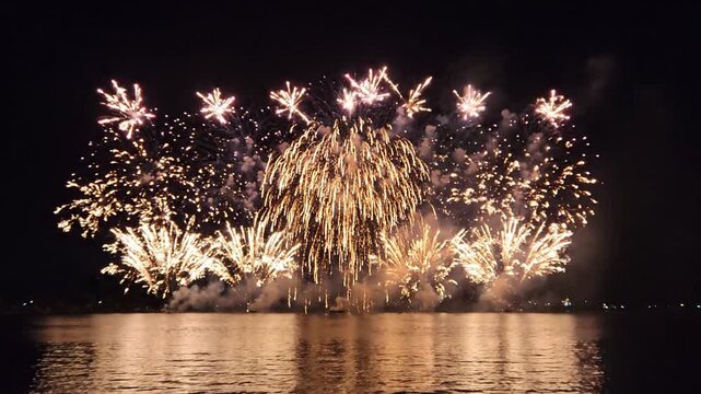 Vibrant multi-colored fireworks explode over dark water at night celebration