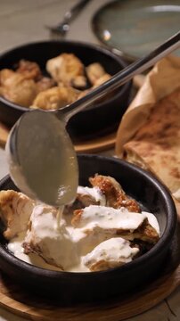 Pouring Creamy Garlic Sauce Over Roasted Chicken in Clay Pot