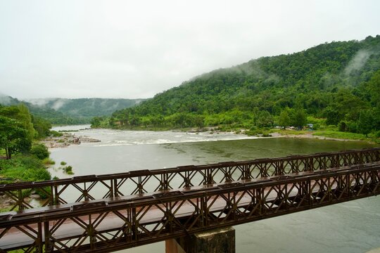 Rustic Metal Bridge Over River Surrounded by Lush Green Hills