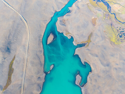 Aerial view of a vibrant turquoise glacial river winding through the barren, volcanic landscape of Iceland.