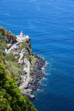Historic Arnel lighthouse perched on steep volcanic cliffs above the blue ocean in Sao Miguel island