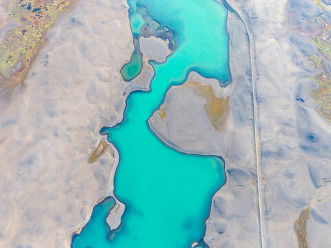 Aerial view of a turquoise glacial river winding through a barren volcanic landscape in Iceland.