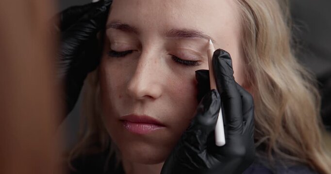 Slow motion close up woman receiving eyebrow mapping and drawing in beauty studio by gloved technician before permanent makeup.